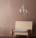 taklampa i stilren klarglas och rund design i ett rosa rum ovanför en trä stol